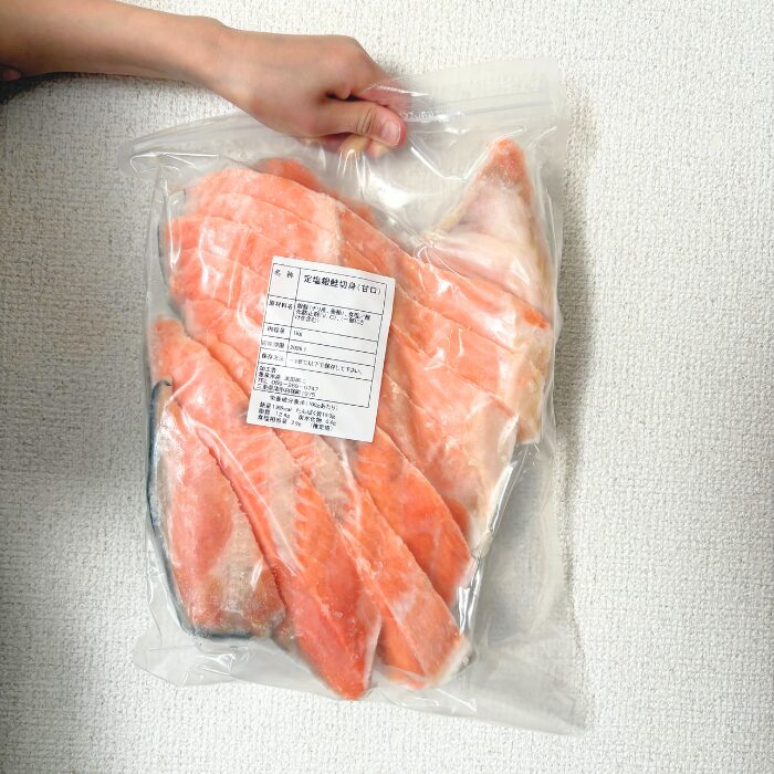 冷凍された訳あり銀鮭の大袋を手に持っている写真。鮭の切り身がたっぷり入っている。